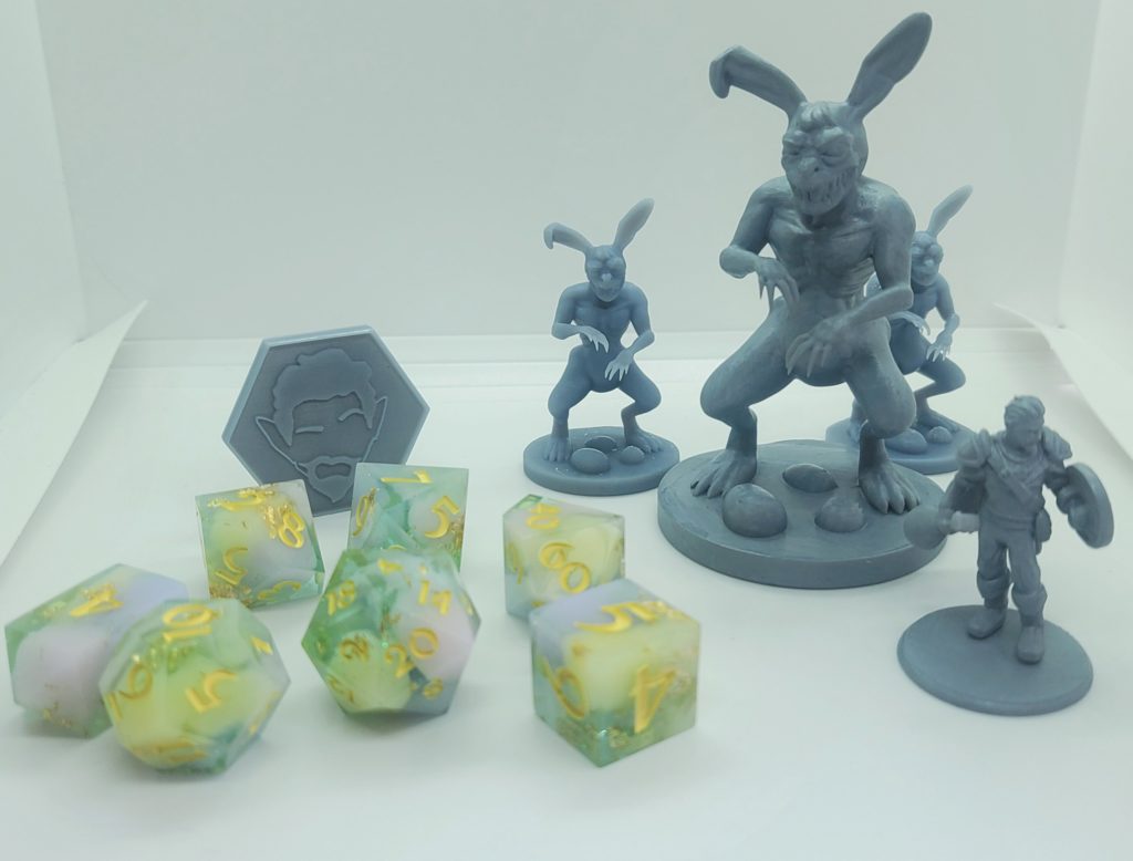 A collection of things in the giveaway. A set of polyhedral dice, three monster rabbit miniatures (one large and two medium) and a miniature of Epic Fred.