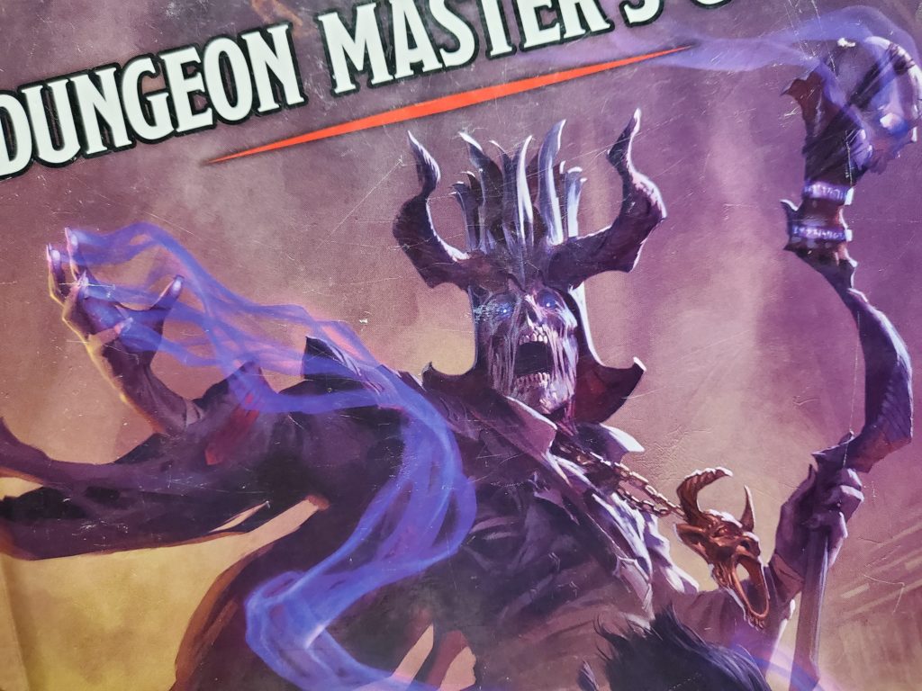 Partial picture of the cover of the fifth edition Dungeon Master's Guide for Dungeons and Dragons. Shows the lich Acererak. He's a skeletal wizard wearing robes. He has a large, horned hat, a gnarled staff and whispy purple magic coming off of his other hand.