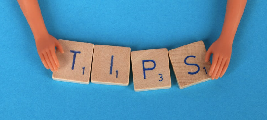 Scrabbble pieces spelling out the word "tips" and held between two doll hands.