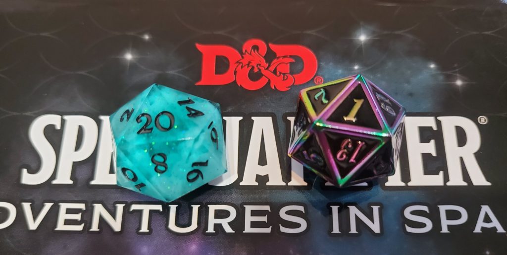 A picture of the cover of "D&D Spelljammer: Adventures in Space" with two 20-sided dice sitting on it. A teal one with the 20 side up, and a black metal one with the 1 face up.